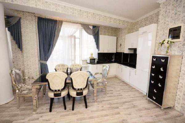 В кухонной зоне установлен белый глянцевый гарнитур и комплект мебели – стол и стулья